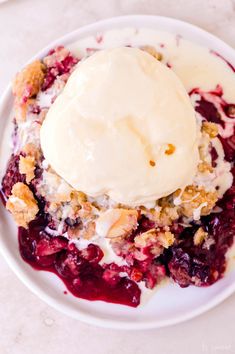 a white plate topped with fruit covered in ice cream on top of a marble table