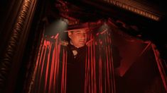 a man standing in front of a mirror with red light coming from behind the curtain