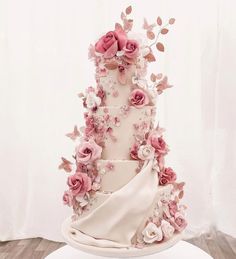 a three tiered wedding cake with pink flowers and butterflies on the top, in front of a white backdrop