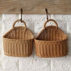 two wicker baskets hanging on a brick wall with wooden hooks in front of them