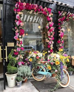 a blue bicycle with flowers on the front parked in front of a flower shop window