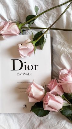 the book dior catwalk is surrounded by pink roses on a white bed sheet