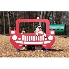 two dogs sitting in the back of a red truck shaped play structure with trees and playground equipment behind it