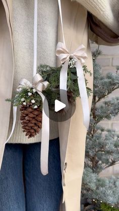 a woman wearing jeans and a sweater holding a pine cone ornament