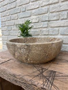 a stone bowl sitting on top of a wooden table next to a brick wall and potted plant