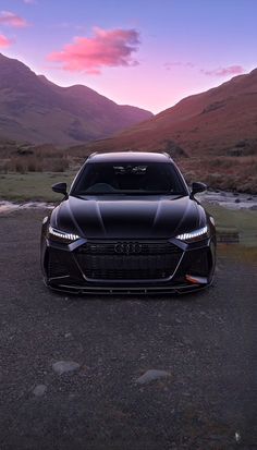 a black car parked on the side of a road in front of mountains at sunset