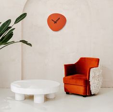 an orange chair sitting next to a white table in a room with a clock on the wall