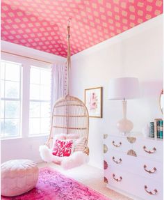 a pink and white bedroom with a hanging chair, chest of drawers, mirror and dresser