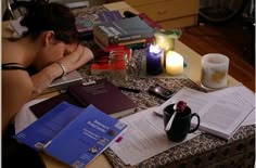 a woman sitting at a table with several books and candles on top of her desk