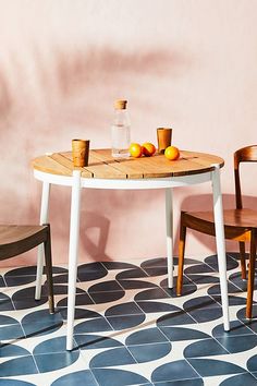 two chairs and a table with oranges on it in front of a pink wall