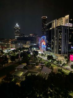 an aerial view of a city at night with ferris wheel in the foreground and buildings lit up