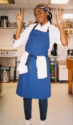 a woman standing in a kitchen with an apron on and her hands up to the side