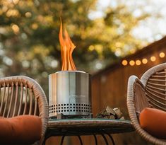 two wicker chairs sitting next to each other near a fire pit on top of a table