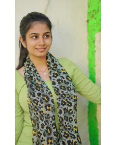 a woman standing in front of a wall wearing a leopard print scarf and green shirt