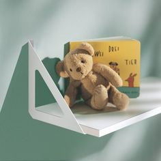 a teddy bear sitting on top of a shelf next to a book