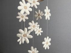 a mobile with white flowers hanging from it's sides on a gray wall next to a plant