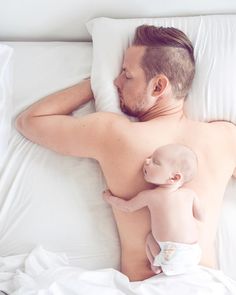 a man laying in bed holding a baby next to him on top of a pillow