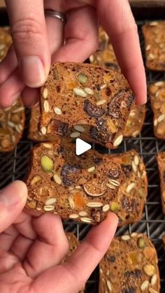 two hands holding up some food on top of a cooling rack with nuts and raisins