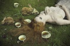 a woman laying in the grass with tea cups and bunnies around her, surrounded by rabbits