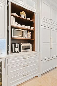 a kitchen with white cupboards filled with appliances and coffee pots on top of them