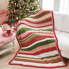 a living room with a christmas tree and a crocheted blanket on the couch