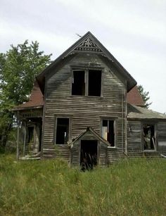 an old run down house in the middle of a field with grass and trees around it