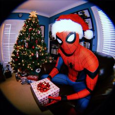 a spiderman sitting in front of a christmas tree with a gift box on it