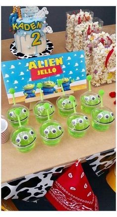 a table topped with lots of green cups filled with cake next to a sign that says alien hello