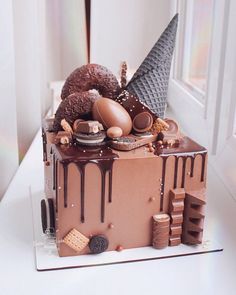 a cake with chocolate icing and various items on it sitting in front of a window