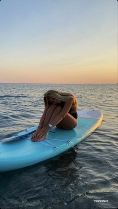 a woman sitting on top of a surfboard in the middle of the ocean at sunset