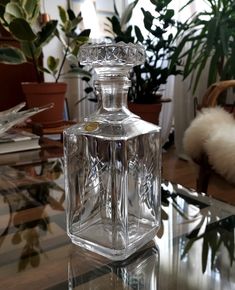 a clear glass bottle sitting on top of a table next to a potted plant