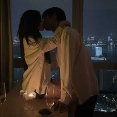 a man and woman kissing in front of a window with the city lights behind them