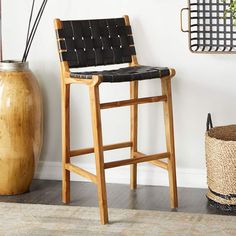 a black leather bar stool next to a brown basket and wall with plants on it