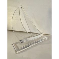 a glass sailboat on a clear base with a white wall in the back ground