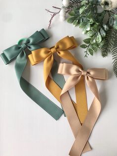 three different colored ribbons tied to each other on a white surface with greenery in the background