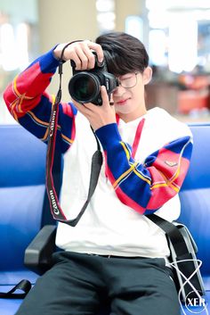 a man sitting on a blue couch holding a camera up to his face with both hands