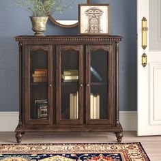 a wooden cabinet with glass doors and bookshelf in the corner next to a rug