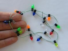 a hand holding a string of christmas lights on a white tablecloth with green, orange and red bulbs