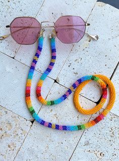 Handmade Beaded Sunglass Strap This sunglass strap is hand made is made out of beads with a very special prison bead technique.It has a tropical vibe with rainbow colours and stripe pattern which gives that contrast look with a tropical design feel. It can be worn in all seasons with all styles. Suitable for casual and occasional wearing. Great boho accessory for Summer and also for winter which beautifully compliments any outfit. The strap is 32 inch ( 81 cm)  long in total. The beaded part is 30 inches. It can fit all sunglass style's sized.  If you are looking for a unique gift this may be the right one for you as it is a rare find. Please do not hesitate to contact me if you have any questions. For other designs, please visit my shop LaPetiteidylleStore on Etsy: https://www.etsy.com/sh Adjustable Multicolor Glasses Chains For Festivals, Colorful Adjustable Glass Beaded Necklaces, Adjustable Round Beaded Chain, Multicolor Beaded Glasses Chains As Fashion Accessory, Multicolor Beaded Glasses Chains For Fashion Accessory, Multicolor Beaded Glasses Chain, Adjustable Beaded Multicolor Glasses Chains, Adjustable Multicolor Beaded Glasses Chains, Beaded Glasses Chains With Round Beads