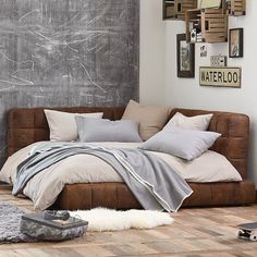 a bed sitting on top of a hard wood floor next to a wall with pictures above it