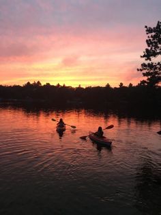 two people are kayaking in the water at sunset