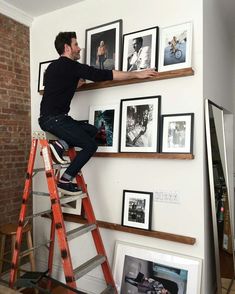 a man sitting on top of a ladder next to a wall filled with framed pictures