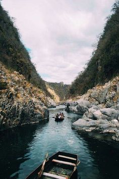 a small boat traveling down a river surrounded by rocky hills and trees on either side