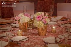 the centerpieces on this table have pink and white flowers in gold vases