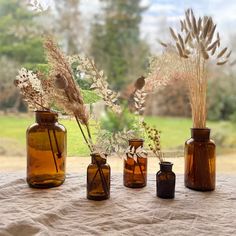 three brown glass vases with dried plants in them on a tableclothed surface