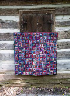 a quilt hanging on the side of a log cabin