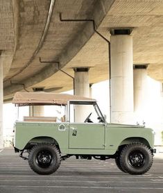 an old green truck is parked under a bridge