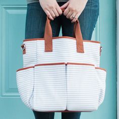 a woman is holding a white and brown striped bag in front of a blue door