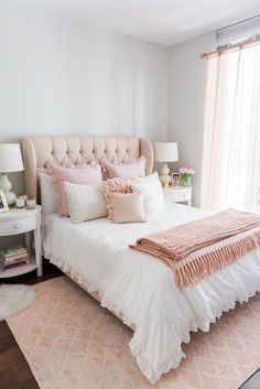 a white bed with pink pillows and blankets on top of it next to a window