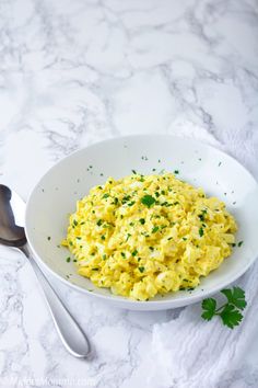 a white bowl filled with scrambled eggs on top of a table next to a spoon